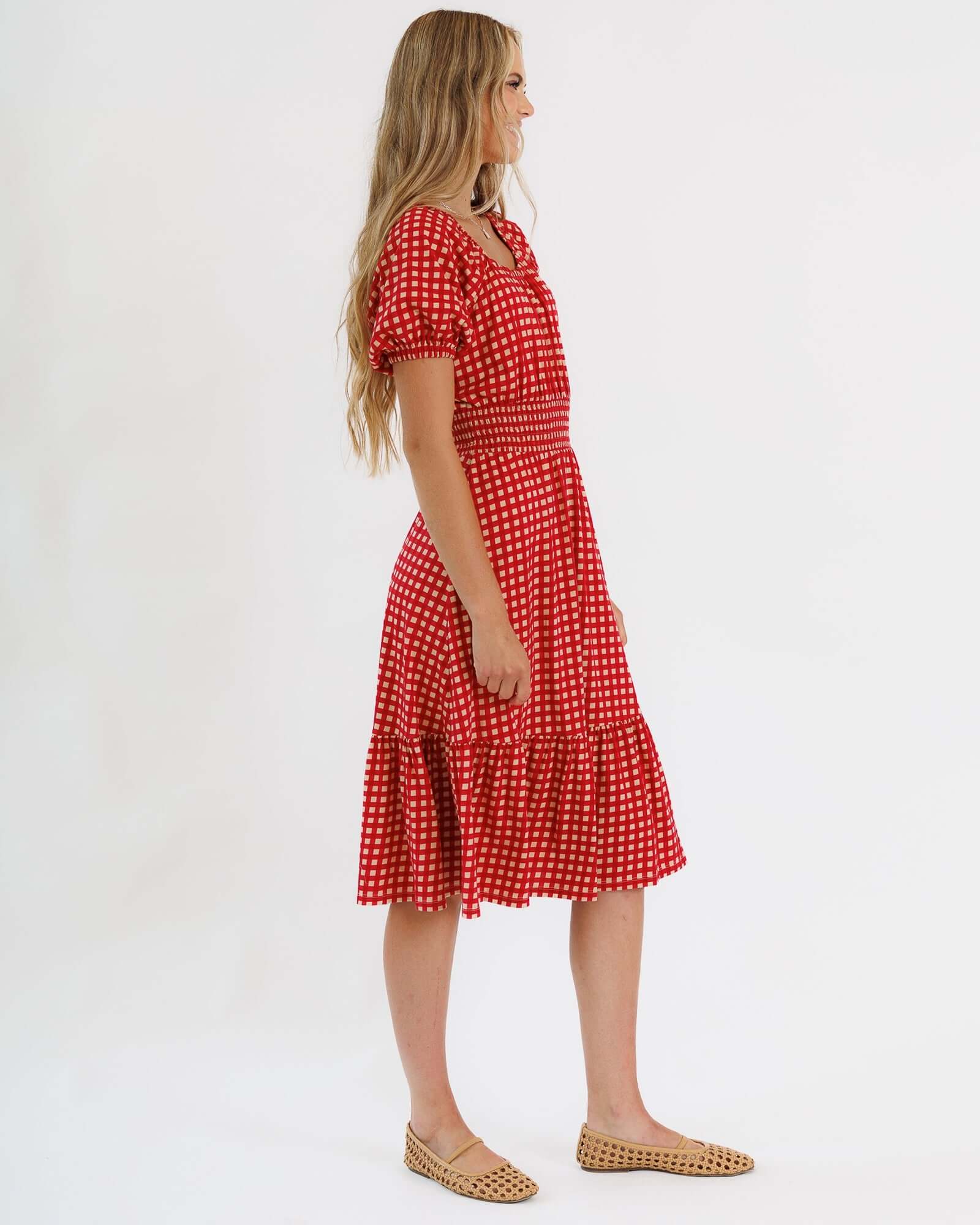Profile view of a model wearing a red polka dot Sweetheart Smocked Dress by Downeast, showcasing its flirty silhouette.