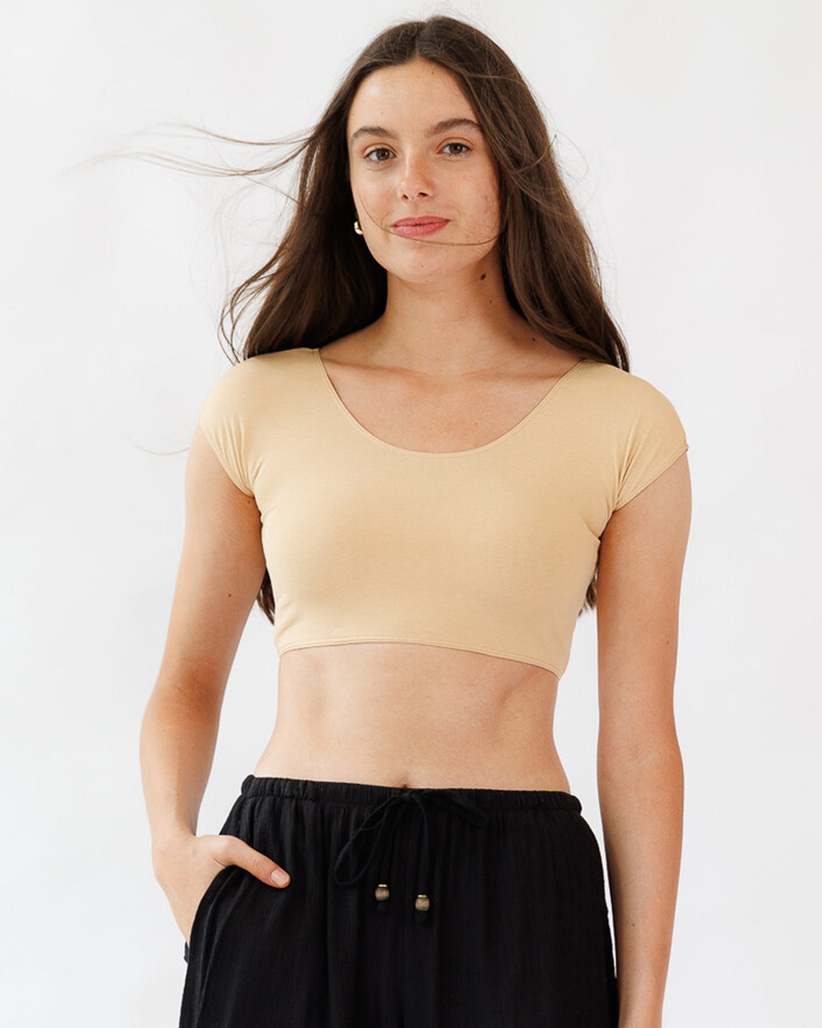 Model wearing Downeast Demi Tee cropped cap sleeve top in beige, showcasing a layered look and comfortable fit.