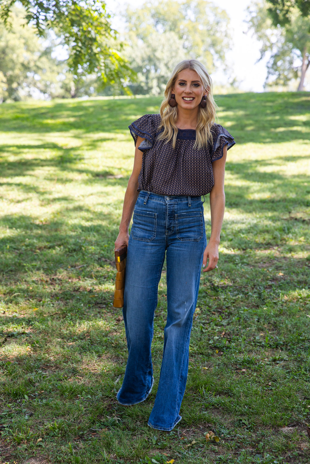 Model wearing James Top Fall Floral Navy Lace Flutter Sleeve with flared jeans in a grassy park.