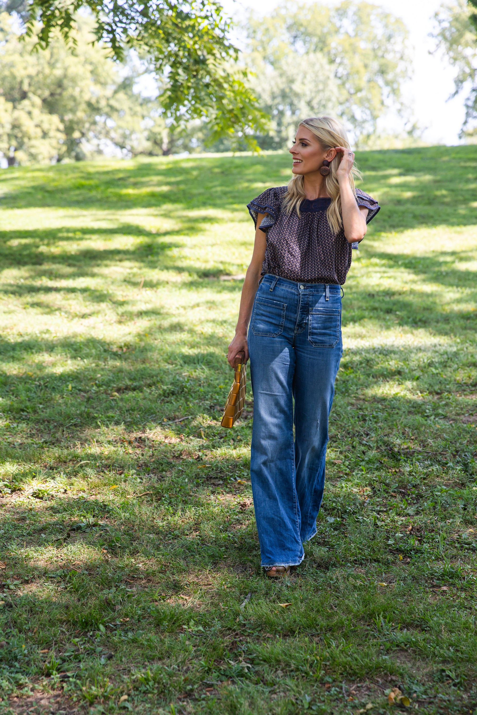 Woman walking on grass wearing James Top Fall Floral Navy Lace Flutter Sleeve with wide-leg jeans.